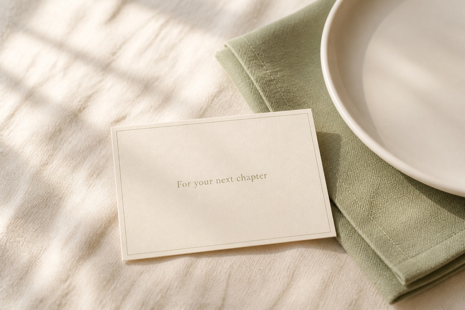 Premier Anniversaire — detail: a cream next-chapter card beside a sage cotton napkin and ivory plate