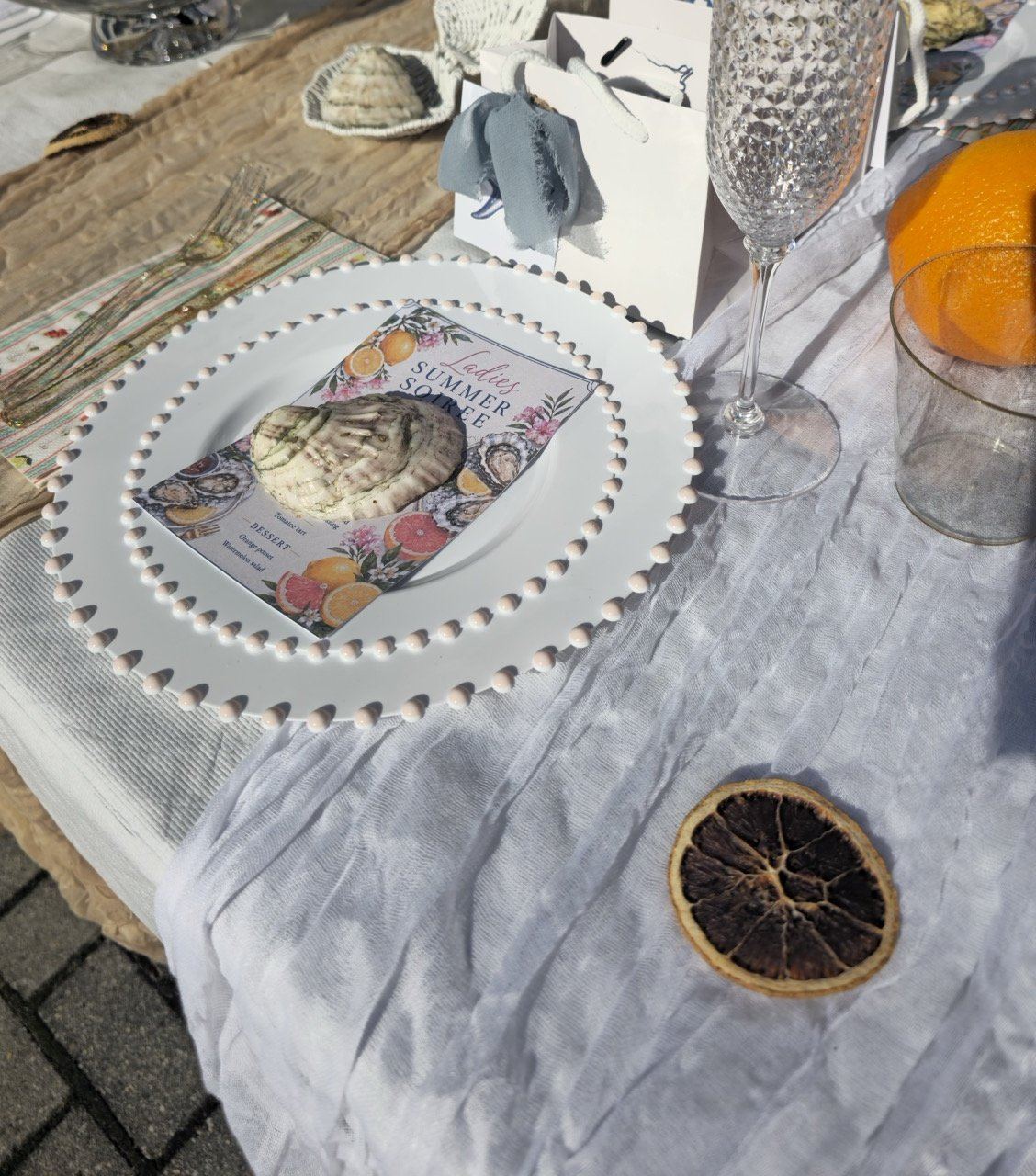 Overhead view of the soirée place setting with menu card, oyster shell, hobnail flutes and favor bags